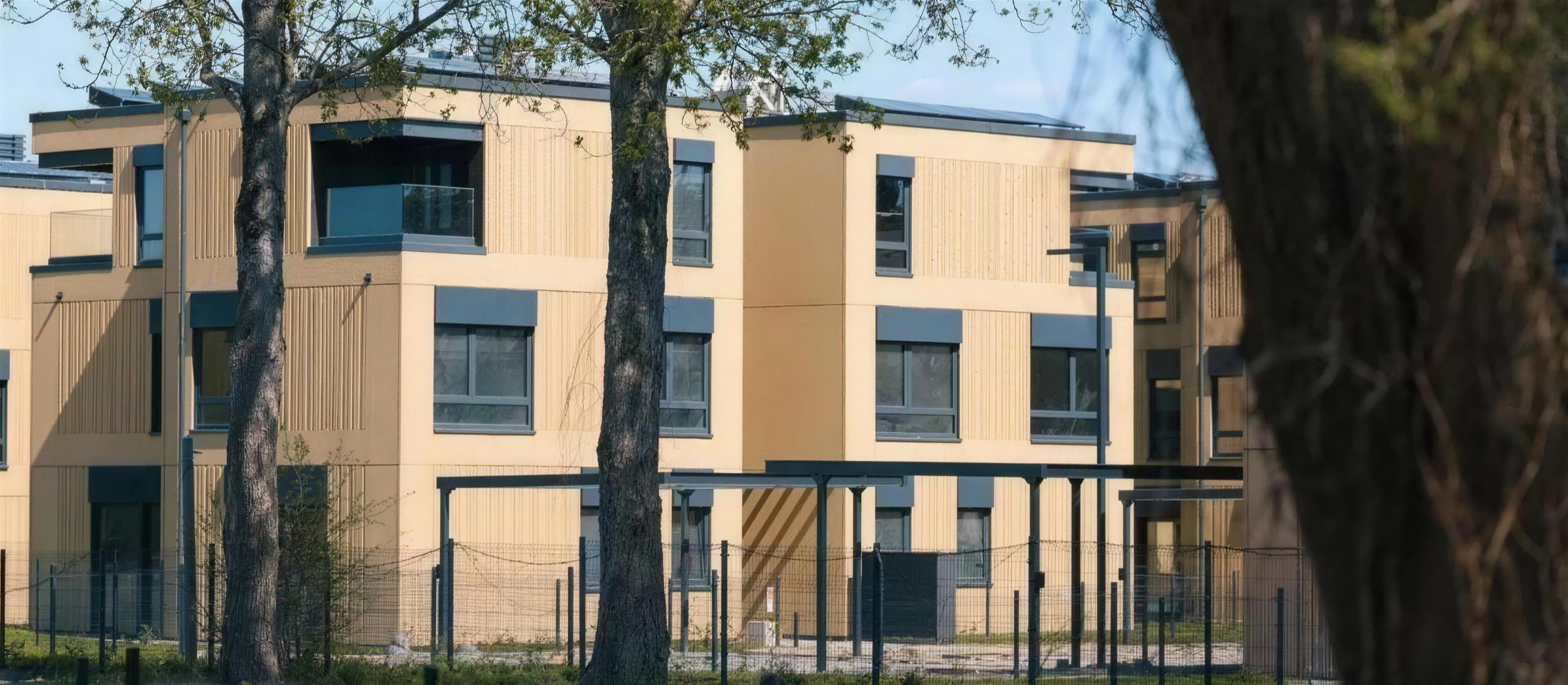 Wohnpark Wola — fertiggestellte Modulgebäude mit Holzfassade zwischen Bäumen